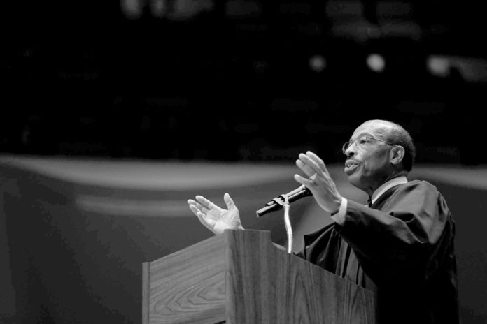 A man in a judges robe speaking with passion behind a podium