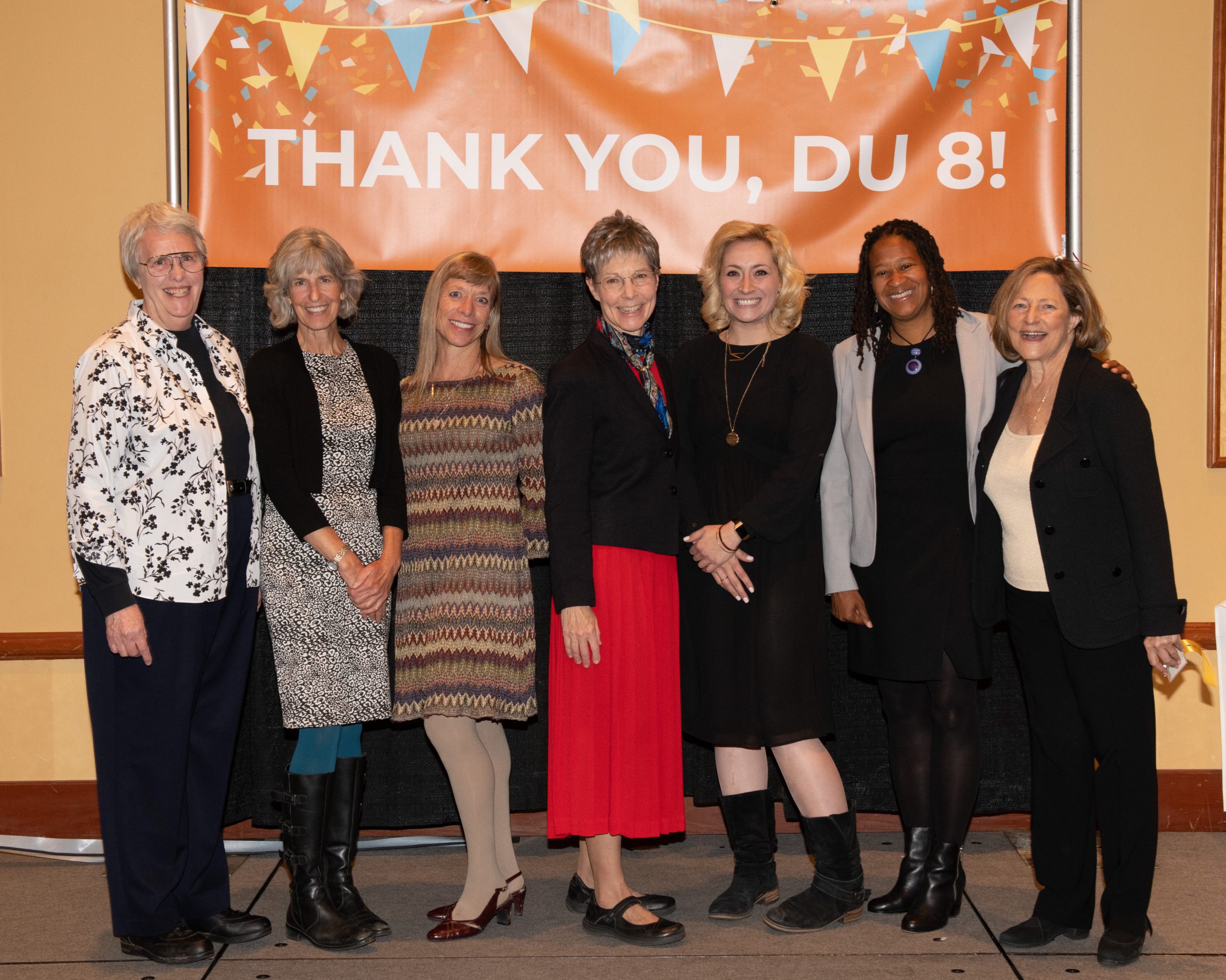 eight women from DU posing for a picture in front of a thank you du 8