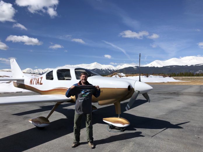 A man standing in front of a small white plane holding up a shirt