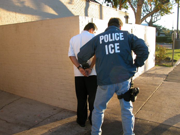 An Immigration and Custom Enforcement Officer arresting a man in a white shirt