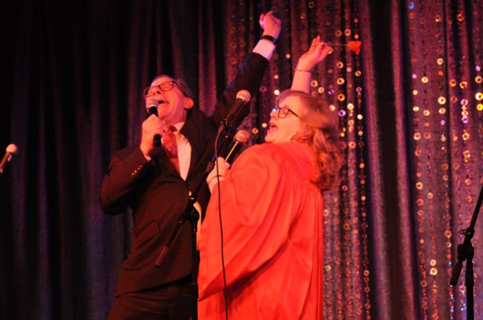 A woman and man throw their hands up in the air while they perform in the 19th “Ethics Revue”