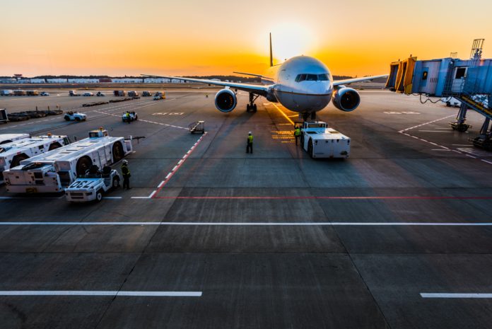 An airplane sits on the tarmac with luggage tugs nearby