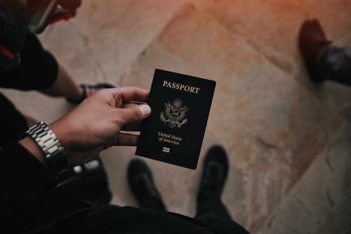 Someone looks down at a passport they're holding nearby a set of luggage.