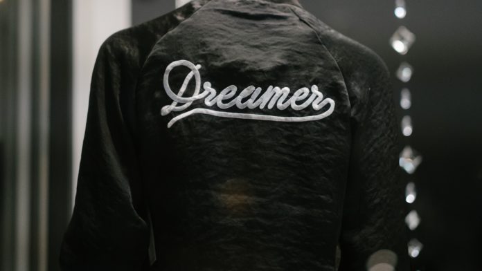 Someone faces away wearing a Dreamers jacket.