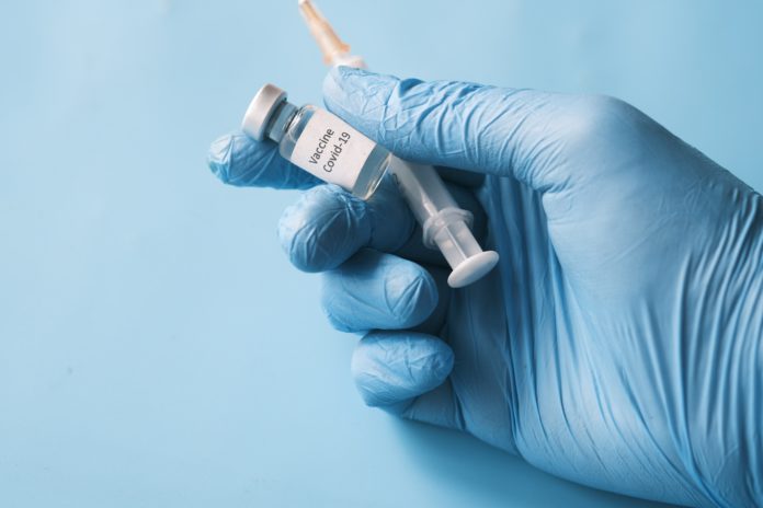 A gloved hand holds a vaccine and needle.