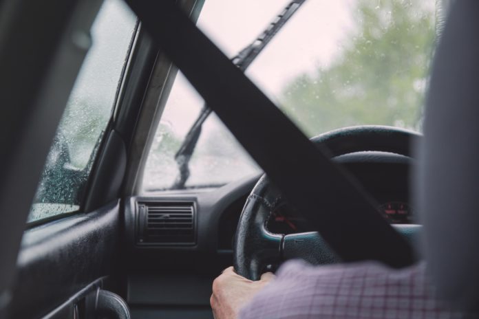 A seat belt is crossed over a driver who is holding the steering wheel steady.