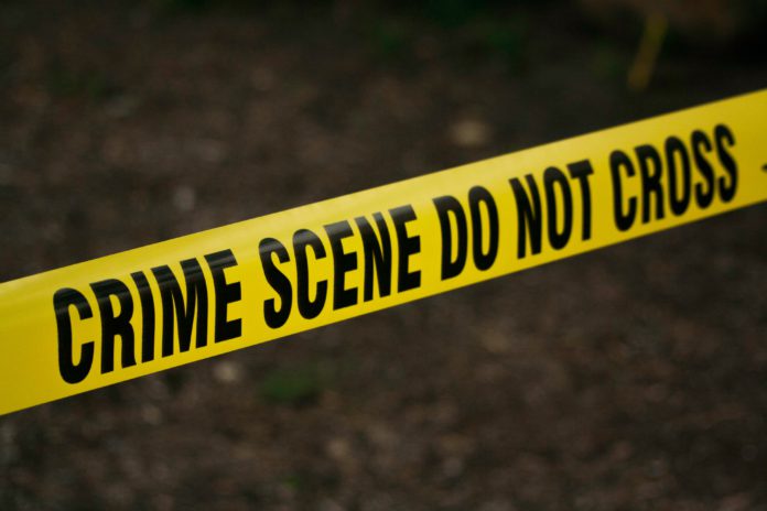 Bright yellow crime scene tape is in focus with a dark, murky background