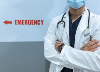 Supreme Court Clarifies Hospital Lien, Medicare Question A doctor stands with arms crossed near a sign for the emergency room.