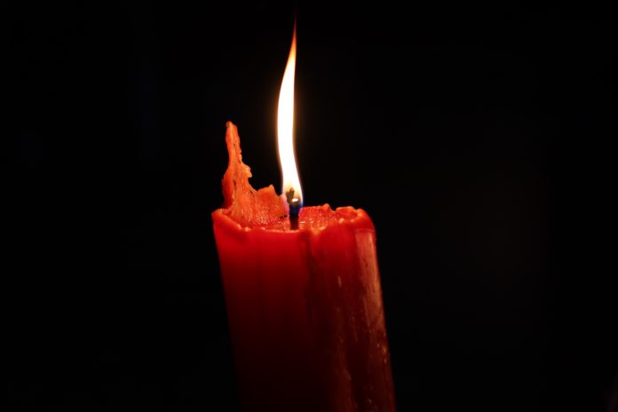 The flame of a red candle flickers in the darkness