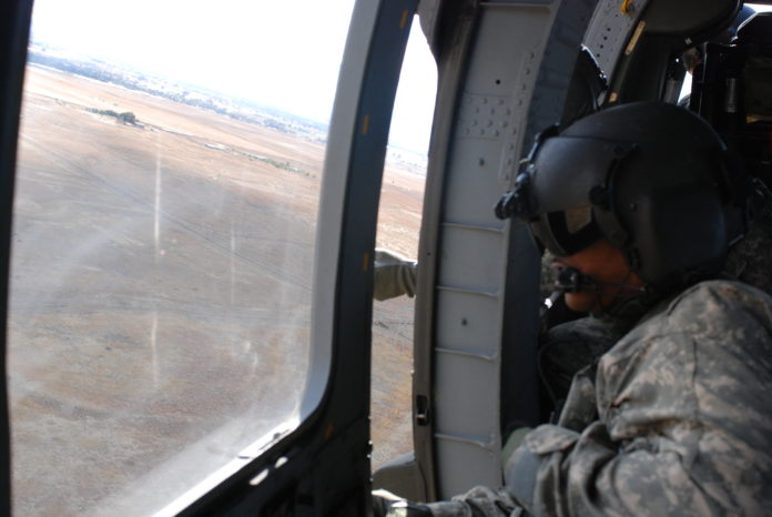 A National Guard Sgt. looks out of a helicopter window intently.