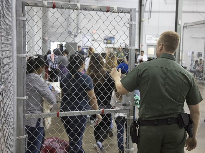 An immigration detention center officer holds a gate open for detainees