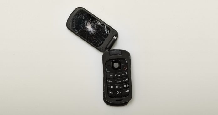 A flip-phone sits ripped in half with a cracked screen.