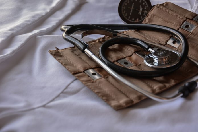 An old stethoscope rests on a leather med kit on clean white sheets.