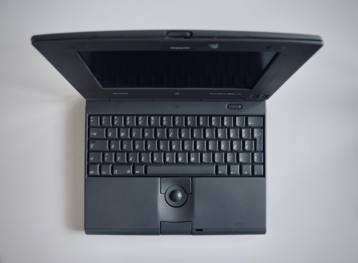 A 1990s laptop sits open on a plain white desk.