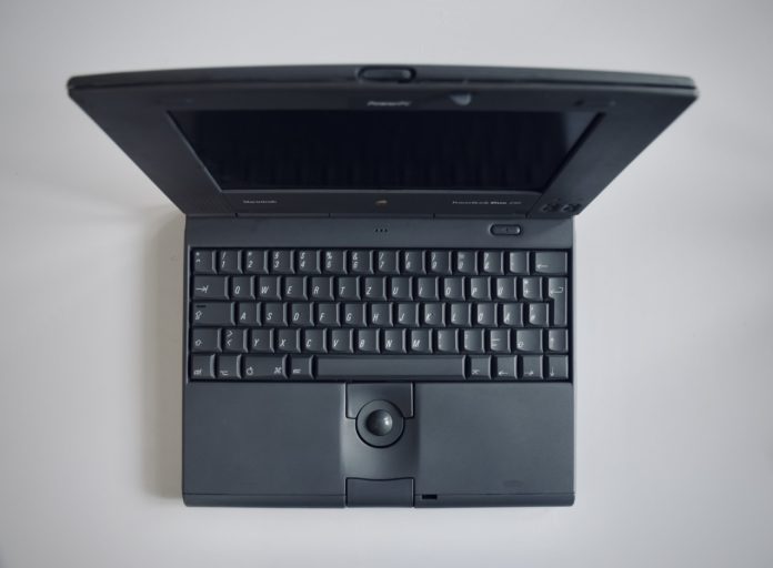 photo-1584985430144-4cb6ffd43f71 A 1990s laptop sits open on a plain white desk.