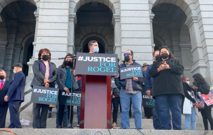 A man speaks at pedestal with people behind him at a rally on the Colorado State Capitol steps .