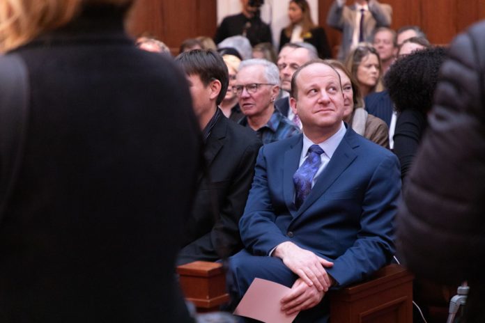 Jared Polis sits on a courtroom audience bench
