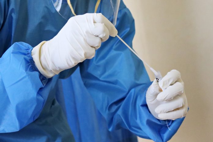 Person in personal protective equipment places swab in test tube.