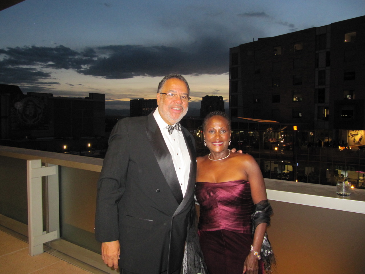 A man and a woman stand close to each other in front of a view of Denver