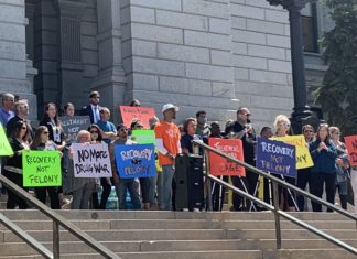 Fentanyl Bill Stalls in Senate Judiciary Committee After Testimony and Opposition Rally A group of people hold signs behind a man speaking at a podium on top of stone steps