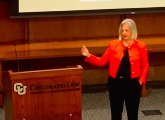 Annual Schultz Lecture Hosts Audrey Zibelman on How Tech Can Accelerate Decarbonized Electric Grids A woman with short, gray hair in an orange blazer speaking next to a podium with the University of Colorado Law School printed on it.