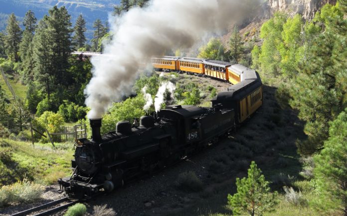 A coal train towing passenger train cars in the mountains