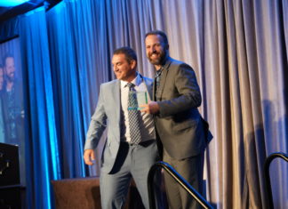 Ross Ziev Wins CTLA ‘Case of the Year,’ Michael Burg and Others Recognized at Annual Awards Banquet A man in a light gray suit with his arm on a man in a dark gray suit who is smiling at the camera and holding a glass award on a stage.