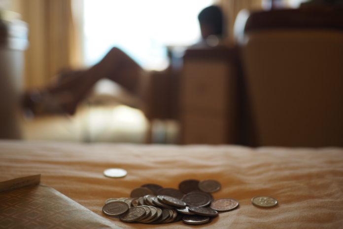 coins sit atop cloth on a table, in the background someone is reclined on a couch.