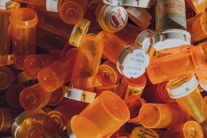 A pile of empty, orange prescription bottles most without labels and a few with unreadable labels.
