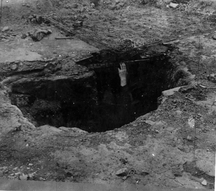 A black and white photo shows a darkened pit with a hand reaching out toward the edge. It's too dark in the pit to see anything else.