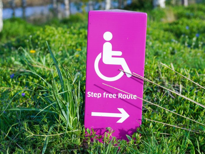 An image of a pink sign in grass indicating wheelchair accessibility.