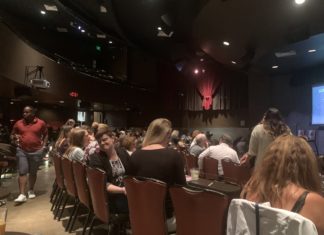 No Kidding: CWBA Hosts Post-Dobbs Public Policy Fundraiser An empty stage surrounded by a crowd of people sitting in chairs in front of small tables.
