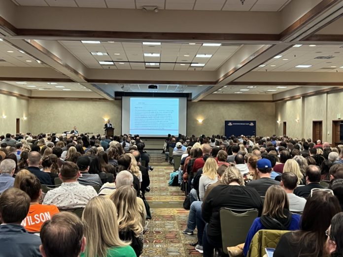 People sitting in a large room, facing a projected screen on the far wall.