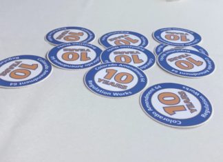 What’s the Future of Legal Cannabis?: Lawmakers Reflect 10-Years After Amendment 64 A white table cloth with ten blue and orange circular stickers with the message Colorado Amendment 64 10 Years Regulation Works.