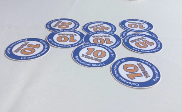 A white table cloth with ten blue and orange circular stickers with the message Colorado Amendment 64 10 Years Regulation Works.