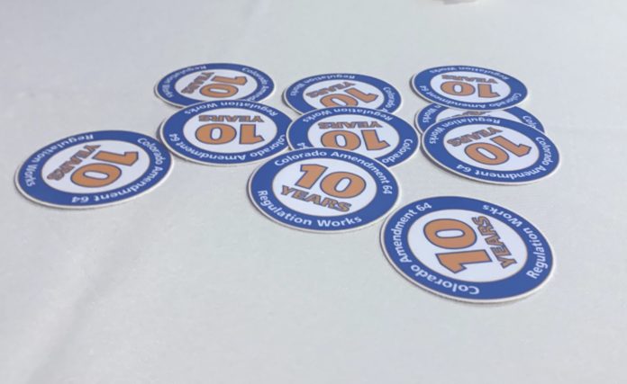 IMG_5059 A white table cloth with ten blue and orange circular stickers with the message Colorado Amendment 64 10 Years Regulation Works.