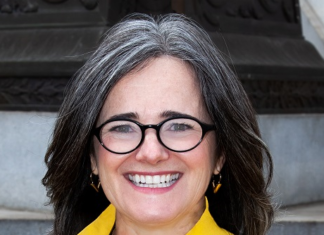 Denver City Attorney Bronson to Resign, Tipper Nominated as Replacement A woman in a yellow coat stands in front of some concrete steps. She wears glasses.