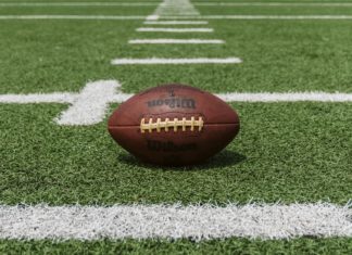 Sports Betting Has Been Jackpot in Colorado A brown football rests between yard lines on a football field. The brand name Wilson can be read on the football.