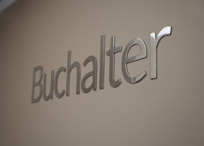Silver chrome letters on a white wall spell out Buchalter.
