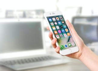 Attorney General Releases Second Draft of Colorado Privacy Act A hand holds a white iPhone with a home screen in front of a blurred background of an office and laptop.