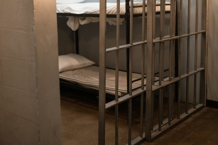 A jail cell is glimpsed through a slightly open cell door