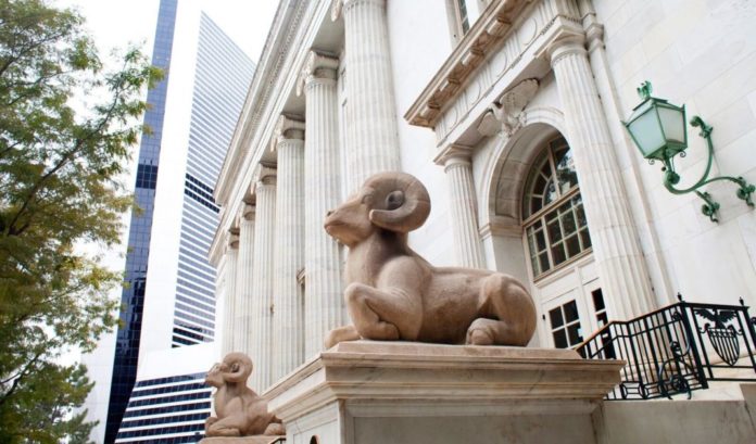 A white courthouse with stone statues of big horn sheep in front of it.