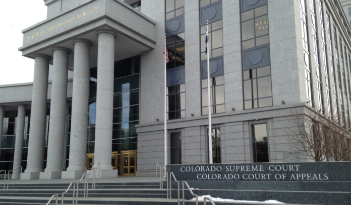 A large building made of concrete has multiple windows and has large columns at the front. Near the front entrance a sign reads “Colorado Supreme Court” and “Colorado Court of Appeals.”