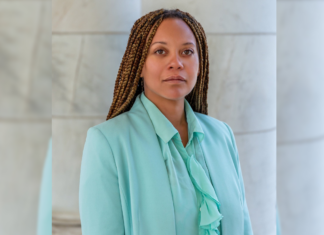 Solo Spotlight: Rachel Robinson Looks to Bring Trauma-Informed Approach to Law A Black woman with braids wearing a teal suit looks straight ahead in front of white pillars.