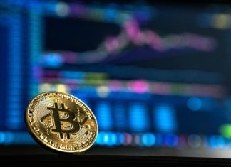 Experts Weigh in on Cryptocurrency Law A gold coin with the letter “B” with two lines going through it can be seen. In the background is a blurred out line chart graph on a computer screen.