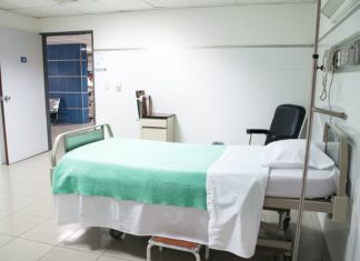 New Report Shows Colorado Hospital Profits Remain High a hospital bed lies empty; just outside the room, health care workers are looking at files.
