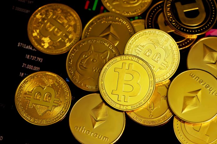 Different cryptocurrencies shown in the form of coins, which are gold in color, are strewn about. What appears to be a bar chart is seen in the background.
