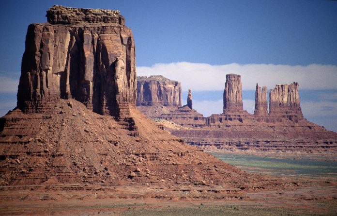 A landscape in the American southwest of a large, orange rock formation with other rock formations in the background.