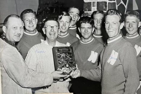 Gardner Paul Smith is holding what looks like an award alongside others in matching sweaters. He’s smiling wide.