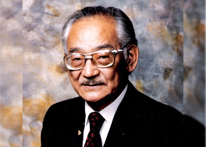 Min Yasui Close Up A man with graying hair wears glasses poses for a picture wearing a suit.